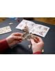 Ръцете сглобяват 3D дървен пъзел Ugears - Дракон, 141 части, със сложни елементи и книжка с инструкции, разпръснати на масата на заден план.-6-thumb