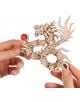 Две ръце държат 3D дървен пъзел Ugears - Дракон, 141 части - малък, детайлен дървен дракон със сложни люспи, изразителна отворена уста и червена сфера в нокътя. Този пъзел е истинско произведение на изкуството.-3-thumb