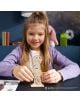 Младо момиче с дълга руса коса се усмихва, докато сглобява 3D дървен пъзел Ugears Хари Потър - Хари, 5 части на маса. Списание и етажерка за книги на заден план добавят магьоснически чар на света.-6-thumb