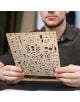 Човек държи лазерно изрязан дървен лист със сложни части от 3D дървен пъзел Ugears - Стиймпънк подводница, 200 части, идеален за сглобяване на този подробен модел на подводница от типа "направи си сам".-3-thumb