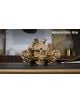 The 3D дървен пъзел Ugears - Стиймпънк подводница, 200 части, с механизъм с зъбни колела и ластици стои на маса. Логото на UGEARS е горе вляво, надписът Assemble me - горе вдясно. Фонът е леко размит.-5-thumb