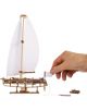 Една ръка сглобява 3D дървен пъзел Ugears - Яхта Ocean Beauty, 95 части, като добавя малък флаг на кърмата. Дървен модел и неговите части са изобразени на бял фон.-4-thumb