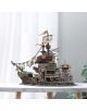 The 3D пъзел Cubic Fun - Пиратски кораб Тортуга, 218 части, е детайлен модел на пиратски кораб с оръфани платна и дървени дъски, изложен върху бяла мраморна маса с размит сив фон и зелени листа.-6-thumb