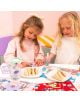 Две млади момичета седят на маса, съсредоточени върху своите Floss & Rock - Enchanted подложка за оцветяване и цветни листове с дейности. Чинии с триъгълни сандвичи, бутилка с вода и стикери допълват това увлекателно занимание за деца.-5-thumb