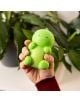 Една ръка държи Legami Антистрес фигурка - Dino, зелена играчка с форма на динозавър, на фона на размазани зелени растения.-4-thumb