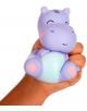 Една ръка стиска Антистрес фигурка Legami - Хипо, сладка лилава играчка с формата на хипопотам, с розови бузки и светлосиньо коремче. Меката играчка е нежно притисната.-2-thumb