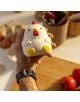 Човек държи Антистрес фигурка Legami - кокошка, сладко, кръгло, бяло пиле с жълти крачета и червен гребен, в кухнята. На заден план са изобразени яйца, прибори и домати. Перфектно като играчка против стрес!.-4-thumb