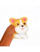 Една ръка стиска Антистрес фигурка Legami - Corgi, сладка жълто-бяла плюшена играчка с формата на корги с големи очи, розови уши и изплезен език, на обикновен бял фон.-2-thumb