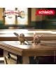 Фигурката на Schleich "Дългопет Фицджералдо" стои върху бюро в класната стая от Училището за магически животни, с логото на Magischen Tiere и Schleich в горните ъгли.-5-thumb