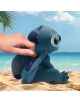 Една ръка поставя монета в Касичка ABYstyle Lilo & Stitch - Stitch, синя касичка, вдъхновена от Lilo & Stitch, разположена на пясъчен плаж с океански вълни - Eдин чудесен подарък за деца.-6-thumb