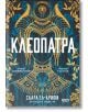 Корица на книгата „Клеопатра“. Този исторически роман се отличава със златисти и сини мотиви, вдъхновени от Египет, богато украсени детайли, както и стилизирани растения и скарабеи върху тъмен фон — всичко това улавя очарованието на египетската царица.-2-thumb