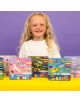 Усмихнато дете с дълга руса коса стои зад жълта маса, на която са изложени цветни кутии Комплект магнитни игри Floss & Rock Fun - Enchanted с игриви мотиви, на лилав фон.-3-thumb