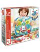 Малко дете се усмихва, докато държи в ръка шарен "Комплект за игра Hape - Експерименти с колела". Кутията показва 115 образователни играчки, предназначена е за възраст 3+ и съдържа STEAM икони.-1-thumb