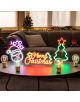 На кръглата маса е поставена LED лампата Legami It's A Sign - Merry Xmas с неонов ефект във формата на лицето на Дядо Коледа, надпис "Merry Christmas", дърво, звезда и празнични лампички. Украсена коледна елха и диван допълват коледна украса.-6-thumb