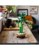 Моделът „LEGO Botanicals Бамбук за късмет“ е поставен в кръгла саксия върху дървена маса в уютна стая, украсена с растения, чаши за чай и зелен фотьойл на заден план.-6-thumb