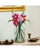 Стъклена ваза с цветни, ръчно изработени хартиени цветя напомня на „LEGO Botanicals: Красив букет с розови цветя“. Тя стои върху мраморна повърхност, а до нея са разположени макари за шиене и декоративна кутия, докато на стената зад нея виси картина в зла-8-thumb
