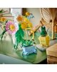 На зелена маса е подреден букет цветя „LEGO Botanicals Малък слънчев букет“ в стъклена кана, както и две малки саксии „LEGO Botanicals“ с симпатични личица – едната синя, а другата жълта, заобиколени от различни декоративни елементи.-7-thumb