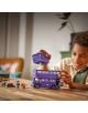 Едно дете се усмихва, докато си играе с комплекта „LEGO Harry Potter: Приключение с автобуса – Полунощният рицар“, сглобявайки лилавия автобус и фигурките върху дървена маса, около която са разпръснати играчки-аксесоари.-6-thumb