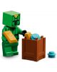 Зелена минифигурка на Крипър от LEGO Minecraft, част от серията „LEGO Minecraft Пустинният патрул на злобарите“, стои до кафяво кашонче, пълно с части от детски конструктор, сред които има и сини и златисти елементи. До кашончето лежи синя LEGO част.-5-thumb
