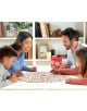 Щастливо четиричленно семейство се събира около маса, играейки на цветната настолна игра Educa - Линкс, 400 картинки. На заден план се виждат рафтове с книги и декорации.-3-thumb