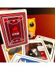 Палуба с настолна игра Exploding Kittens: Котка Burglar Edition стои изправена върху червена повърхност, заобиколена от няколко карти, а жълта фигурка на котка наднича иззад тестето.-7-thumb