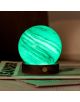 Настолна лампа Gingko AstraGlass Light Mini Polar Cloud се отличава със светещ зелен, ръчно издухано стъкло дизайн с вихрени бели шарки върху тъмна дървена основа с месингов бутон, изложена върху списания.-5-thumb