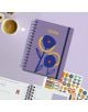 Седмичен тефтер-органайзер Miquelrius Marf Organic Dualidad Floral 2026 с абстрактни сини и жълти цветя на лилава корица е поставен върху лилава повърхност до чаша кафе, стикери за тефтер и отворена страница.-7-thumb