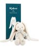 The плюшена играчка Kaloo - зайче, кремаво, 35 см с дълги уши, сини очи и шарен син шал е поставено пред синята кутия Kaloo с илюстрация на зайче-идеална бебешка играчка.-4-thumb