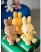 Кремаво-жълто плюшено зайче Miffy Eco Corduroy (23 cm) седи върху яркозелена тръба, а на заден план се виждат още две размазани плюшени зайчета върху синя повърхност.-4-thumb