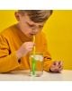 Младо момче с жълта риза отпива ледена вода от прозрачна чаша, използвайки Сламки с променящи се цветове Kikkerland - Червейчета, 6 бр. Жълтият фон придава жизненост, докато той гледа надолу към цветната си сламка.-3-thumb