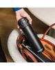 Ръка държи стоманена бутилка Kambukka Elton Insulated Nightfall, 0.600 л, готова да я постави в отворена кафява кожена чанта върху бял текстуриран стол.-7-thumb