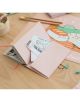 Розов Тефтер за пътуване Grupo Erik - Pusheen Sushi Roll Tripple Travel на дървено бюро държи снимки и билет за пътуване до Токио, а наблизо има пастелни канцеларски материали, илюстрирана папка за суши, молив и щипки за хартия.-3-thumb