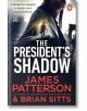 Корицата на книгата "Сянката на президента" изобразява жена в сянка, облечена в тренчкот, на градска улица, със смел бял и червен текст и драматично осветление, което напомня за класически трилър.-thumb