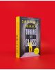 Екземпляр от "Стъкленият трон" (Throne of Glass, Book 1) стои изправен на обикновен червен фон, а на корицата му е изобразена сенчеста фигура сред колони, удебелен текст и златен стикер "световен бестселър".-2-thumb
