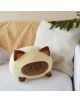 Възглавница Балви - Котка, кафява - мека кръгла котешка възглавница с кафеви уши, лице и лапи стои на бял диван до бяла възглавница и бежово одеяло. Идеална за подарък, със зелено растение на заден план.-4-thumb