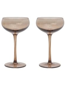 Две елегантни The Lou Coupe чаши за коктейл с широки, плитки чаши и дълги, тънки дръжки стоят една до друга на бял фон. Предлагат се в книжарница Orange.
