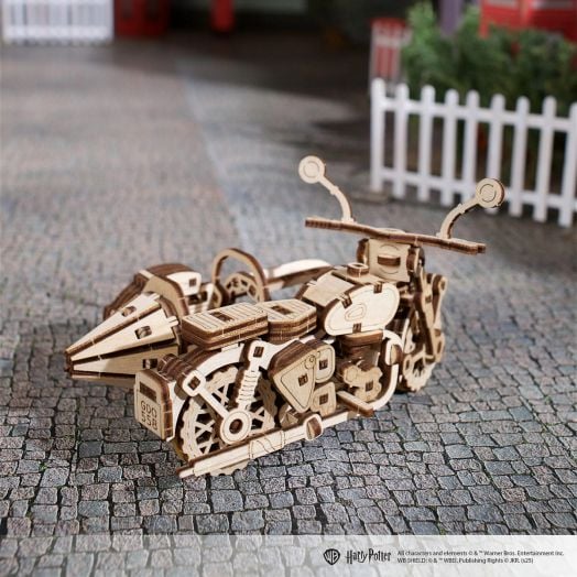 3D дървен пъзел Ugears Хари Потър - Летящият мотор на Хагрид, 130 части, с фини лазерно изрязани детайли, е изложен върху павирана повърхност с дървена ограда на заден план.-7