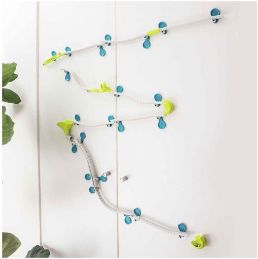 Детската игра Kosmos - Gecko Run Big Box е монтирана на бяла стена, с гъвкави писти, сини вакуумчета и зелени и жълти фунии; в долния ляв ъгъл се вижда зелено листно растение.-3