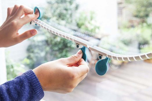 Ръце, прикрепящи бял пластмасов перваз със сини вендузи от комплекта Детска игра Kosmos - Gecko Run Big Box към прозорец, като през стъклото се вижда размазана градина навън.-4