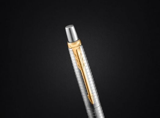 Химикалката Parker Jotter Special Edition 70th Anniversary GT в сребрист металик с текстуриран корпус и златен клипс във формата на перо е изобразена на плътен черен фон.-3