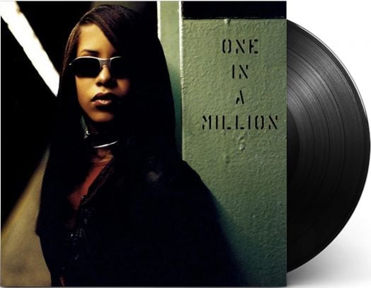 Жена със слънчеви очила стои до зелена стена с надпис "One in a Million"; сцената, вдъхновена от Aaliyah - One In A Million (2 VINYL), показва част от виниловата плоча на албума, която се вижда вдясно.