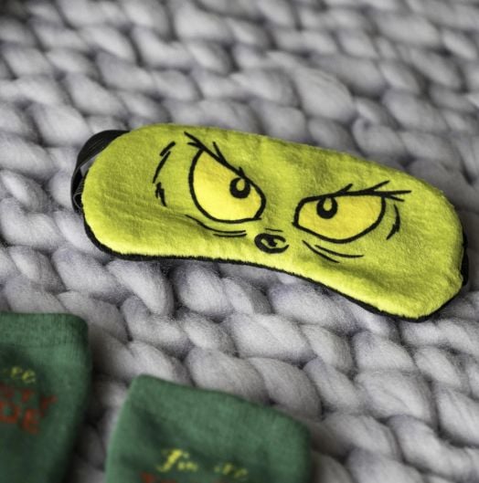 Уютен коледен комплект с Fizz Creations - Гринч: жълта маска за сън с гневни очи на Гринч върху дебело сиво плетено одеяло, плюс зелени меки чорапи, които се виждат частично наблизо - идеално за феновете.-4