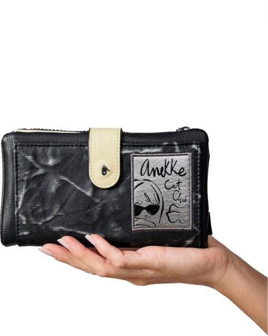 Една ръка държи дамски портфейл Anekke Memories Towanda (18 x 10 x 2 см) с лека закопчалка и лепенка с илюстрация на котка и текст "AnkKe Cat Club" отпред, вдъхновен от Anekke Memories.-9