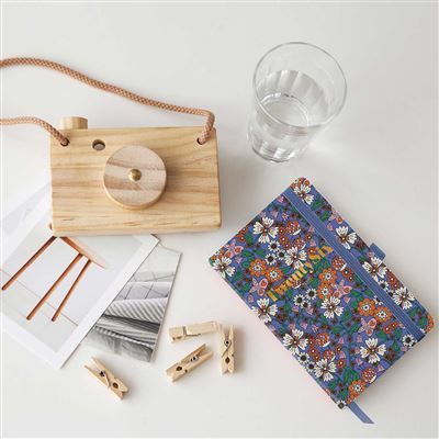 Дървен фотоапарат-играчка, чаша с вода, Джобен тефтер - Оргайзер Miquelrius Natura Blooming 2026, тетрадка с флорален десен и цип, дървени щипки и две отпечатани снимки са подредени върху бяла повърхност.-4