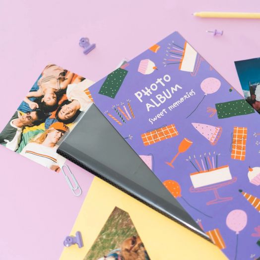 Фотоалбумът Grupo Erik - Sweet Memories, за 96 снимки 10x15 см, е отворен върху розова повърхност с разпръснати снимки, кламери и декорации - идеален за съхранение на спомени.-5