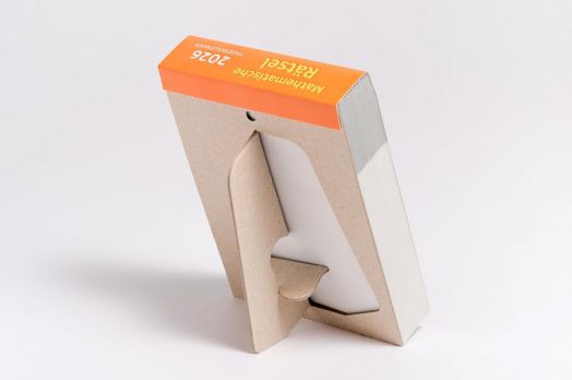 Дебела книга с оранжева корица, озаглавена "Heureka Mathematische Rätsel 2026: Tageskalender mit Lösungen", стои изправена в специално изрязан картонен държач, идеален за феновете на Mathematische Rätsel.-3