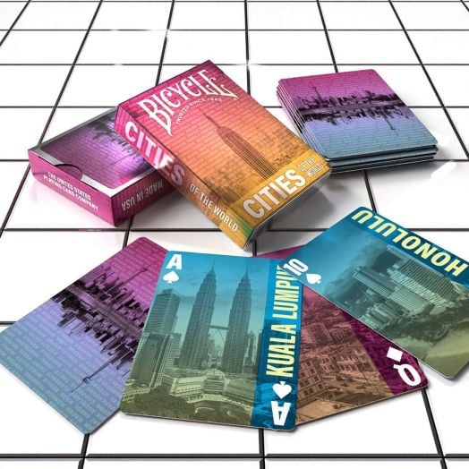 Тестето карти за игра Bicycle Cities of the World е изложено върху бели плочки, като показва ярки карти със забележителности от градове като Куала Лумпур и Хонолулу, всички с характерното покритие на въздушната възглавница.-6