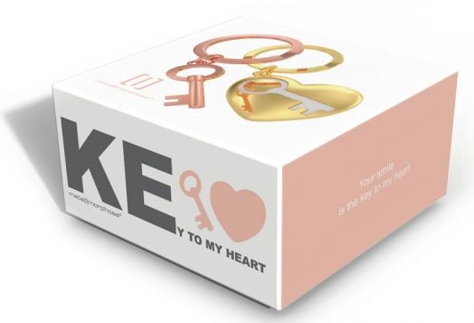 Кутия за подаръци в бяло и прасковено от Metalmorphose съдържа ключодържател Key To My Heart с илюстрации на сърце и ключ. Напечатани са надписите "KEY TO MY HEART" и "Your smile is the key to my heart" (Твоята усмивка е ключът към сърцето ми).-2