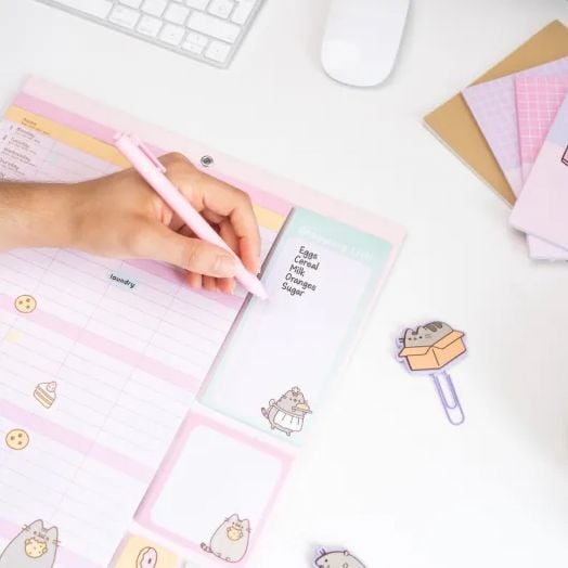 Ръката пише с розова химикалка върху пастелен тефтер, заобиколена от клавиатура, мишка, тетрадки, стикери и щипки със симпатичната котка Pusheen - плюс 16-месечната програма Grupo Erik Pusheen The Cat планер-пад (09/2025-12/2026) за поддържане на организа-5