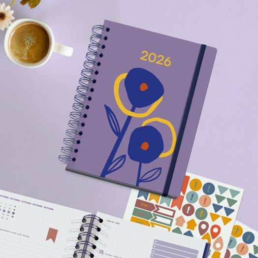 Седмичен тефтер-органайзер Miquelrius Marf Organic Dualidad Floral 2026 с абстрактни сини и жълти цветя на лилава корица е поставен върху лилава повърхност до чаша кафе, стикери за тефтер и отворена страница.-7